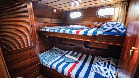 Cabin on Gulet Thalasa with two bunk beds, wood paneling, and porthole windows.