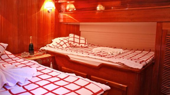 A cabin on Gulet Il Fratello with two single beds, warm wood decor, and a bottle of champagne on a small table.