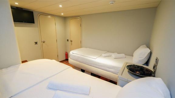 Twin room of the Gulet Vega with two single beds, television and simple furnishings.