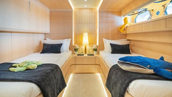 The bright cabin features two single beds, bedside lighting, plush toys and round porthole windows.