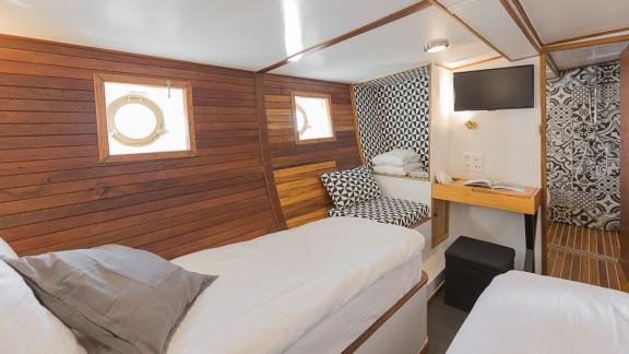 The cabin includes two single beds, a TV, a seating area, a desk and windows.