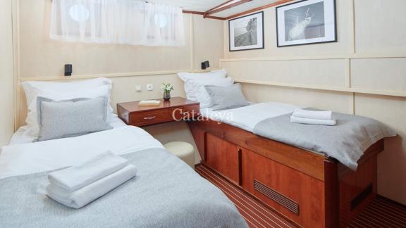 A cabin with two single beds, a desk and decorative pictures, ideal for comfortable nights on the Gulet Cataleya in Croa