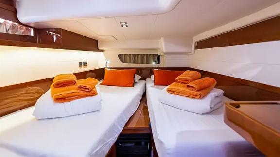 The twin-bed cabin of the Tourbillon yacht offers a cozy stay with orange towels and pillows.