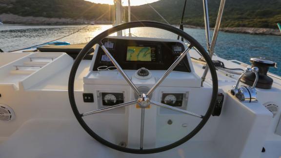 The helm station of a Lagoon 560 catamaran with a sleek steering wheel and modern navigation instruments, overlooking th