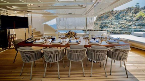 Ariela yacht features a 10-seat elegant dining setup on deck with sea and rocky cliff views in Göcek.