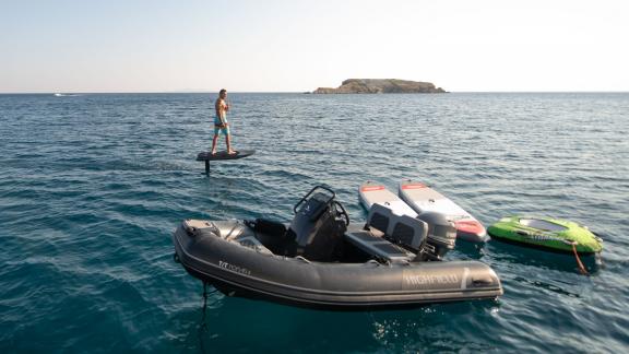 Ein Mann auf einem E-Foil, begleitet von einem Beiboot und Paddleboards, für ultimatives Wassersportvergnügen.