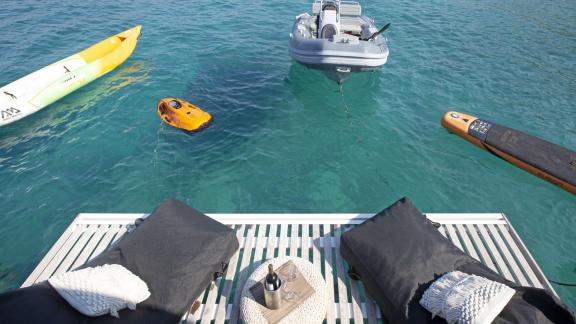 The relaxation area of the Lagoon 560 with two sun loungers, surrounded by a kayak, inflatable boat, and paddleboard on