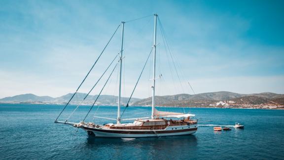 Ein luxuriöses Segelschiff liegt ruhig im klaren, blauen Wasser vor einer malerischen Küstenlandschaft.