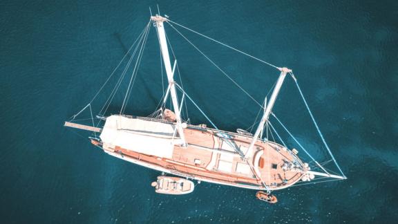 An elegant sailing ship lies calmly in the deep blue water, taken from a bird's eye view.