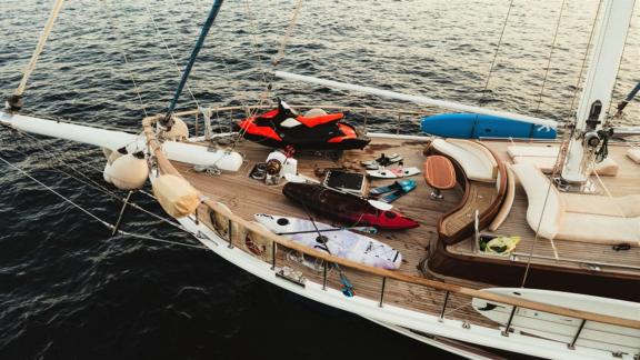 A luxurious sailing boat with kayaks, paddleboards and a jet ski on deck, ready for water sports adventures.