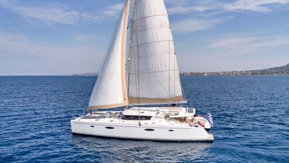 Eleganter Katamaran mit weißen Segeln auf dem blauen Meer vor der Küste Athens.