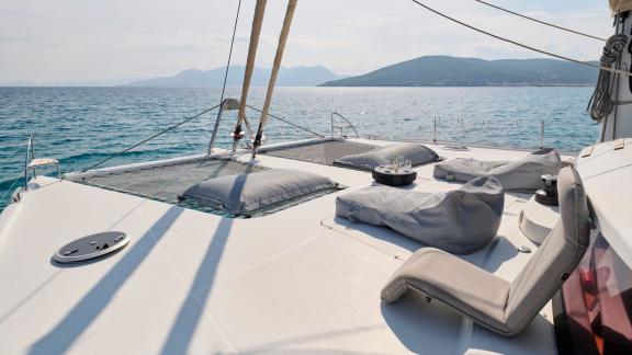 Sonnenliegen und Netze auf dem vorderen Deck eines Katamarans mit Blick auf das Meer und die Berge.