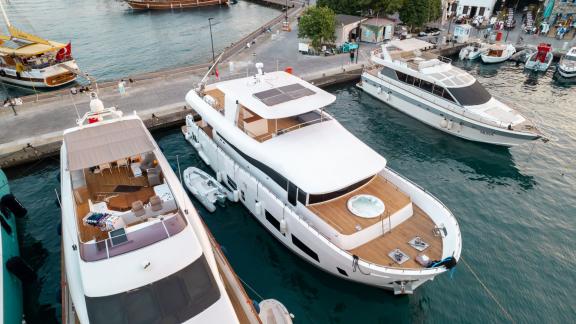 The Almila yacht is docked at the harbor among other yachts, featuring a spacious deck and jacuzzi.