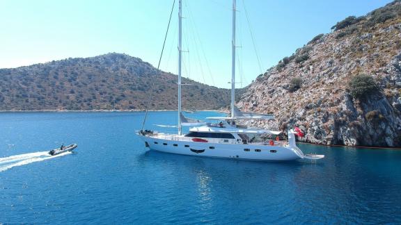 Motorsailer Angelo 3 anchored in a rocky cove, with a boat cruising nearby.