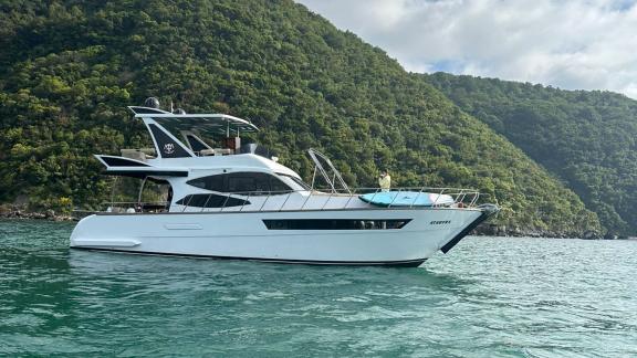 The exterior view of motor yacht Ata Bora in the calm waters of Bodrum in front of green mountains.