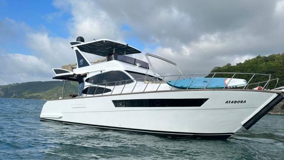 Die Motoryacht Ata Bora steht in Bodrum vor grünen Bergen, auf dem Deck befindet sich ein Paddelbrett.