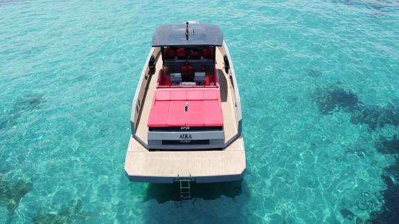 The aft deck of motor yacht Aura features comfortable red seating and a swim ladder in turquoise waters.