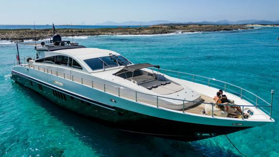 The motor yacht Aya One offers comfortable seating areas on its modern deck while anchored in turquoise waters.