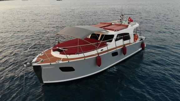 Barbaros 3 lobster yacht rests at anchor in calm Marmaris bay with red cushions.