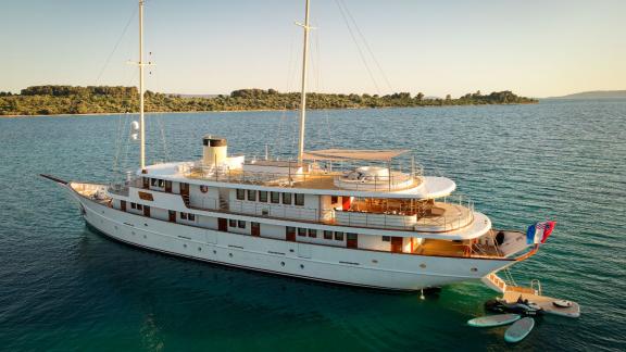 The Bellezza yacht peacefully anchored in turquoise waters, surrounded by green islands and evening sun.