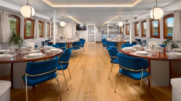 Elegant indoor dining area on the Bellezza yacht with blue chairs and large windows overlooking the sea.