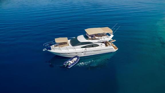 Motor yacht Blue My Story anchored in calm blue waters with a small boat alongside.