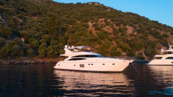 The motor yacht Bormus 2 is peacefully anchored in a bay surrounded by greenery.