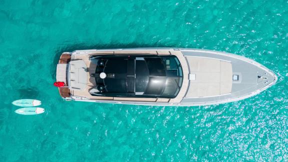 Motor yacht Chilli viewed from above in turquoise waters, with two paddleboards nearby.