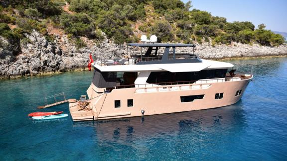 Compass trawler yatı, Göcek'in berrak sularında demirlemiş durumda. Yanında paddleboard ve deniz oyuncakları bulunuyor.