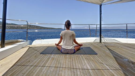 Kadın, arka planda sakin deniz manzarası eşliğinde Crazy Horse Katamaranının güvertesinde yoga yapıyor.