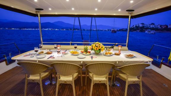 Unter den Motoryacht Charter Optionen in Göcek zeigt Dalibay 2 Achterdeck am Abend mit Esstisch und Sitzplätzen.
