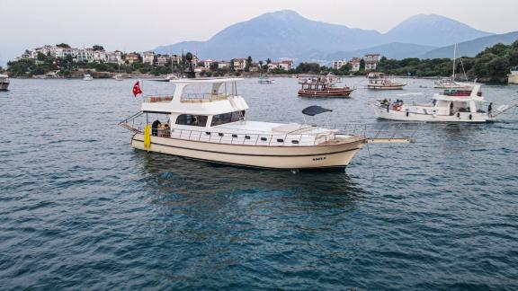 Among motor yacht rental options in Gocek Dalibay 2 is anchored in a calm bay with shoreline and nearby boats.