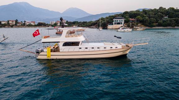 Among motor yacht rental options in Gocek Dalibay 2 is anchored with side view in a calm bay near the shore.