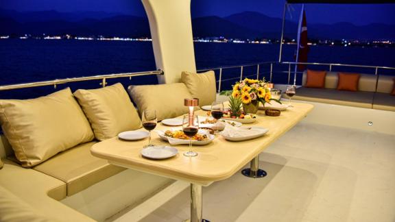 Among motor yacht rental options in Gocek Dalibay 2 upper deck shows evening view with dining table and seating area.