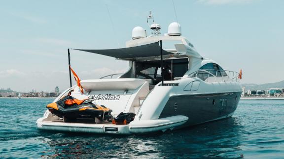 The motor yacht Esperanza is cruising slowly with a jet ski on the aft deck, against a city skyline.