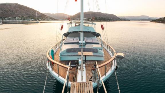 The bow of Gulet Esperanza with comfortable sun loungers aligned in a serene bay at sunset.