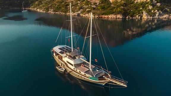 Luxurious Gulet Esperanza anchored in a serene bay with clear blue waters and lush coastal scenery.