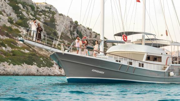 A group of guests enjoys the view from the bow of Gulet Esperanza, surrounded by rocky coastline and clear waters.