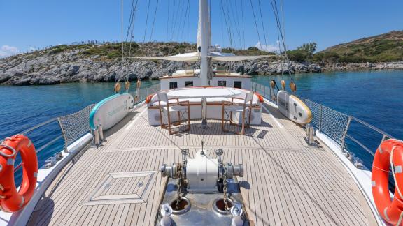 The spacious foredeck of the Gazella gulet features a seating area and tables. Wooden details and a stunning sea view en