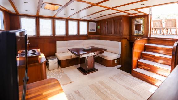 Gazella’s salon features a large corner sofa, a wooden table, and stairs leading to the outer deck.