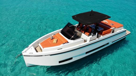 The deck of motor yacht Ikigai, floating in turquoise waters, features orange cushions and a comfortable seating area.