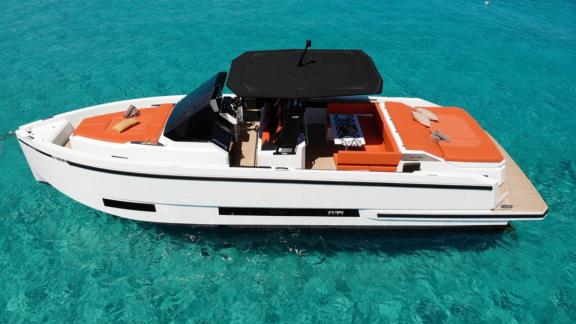 The spacious deck of motor yacht Ikigai, floating on turquoise waters, features a seating area with orange cushions.