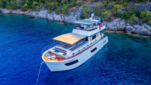 Die Trawler-Yacht Kaan Bey 2 liegt vor Anker in klarem blauem Wasser an einer felsigen Küste.