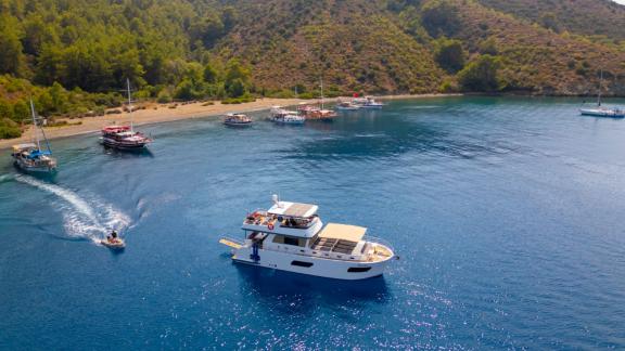 The trawler yacht Kaan Bey 2 is anchored in a cove with other boats.