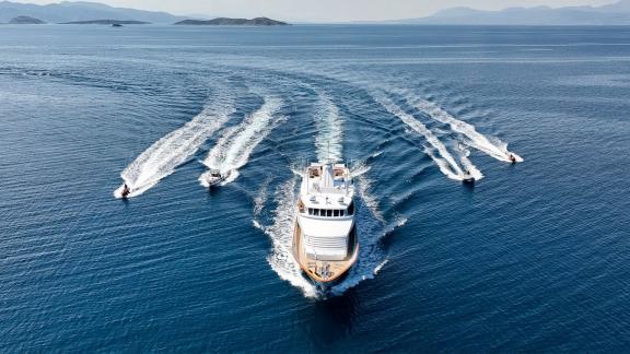 Kokomo Nights cruises off Athens accompanied by jet skis and tenders, creating a dynamic seascape.