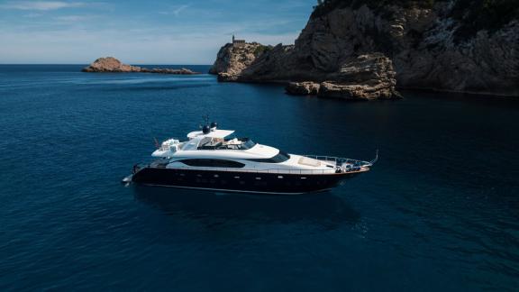 Among Ibiza daily yacht charter options, Lady KC is seen anchored in a calm bay surrounded by rocky shores.