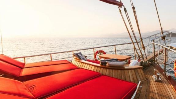 Comfortable red loungers on the deck of a yacht overlooking the vast sea at sunset.