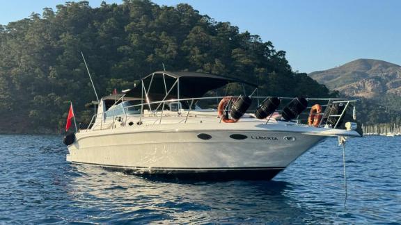 Motoryacht Liberta liegt vor Anker im blauen Wasser mit grünen Bergen im Hintergrund.