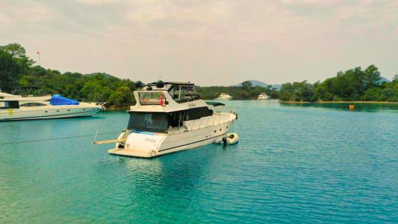 The motor yacht Niloş is moored in a tranquil cove alongside another motor yacht.