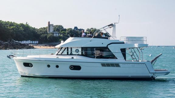 Die Motoryacht Ocean Dreamer fährt in ruhigen Gewässern nahe der Küste, im Hintergrund ein grüner Wald und Gebäude.